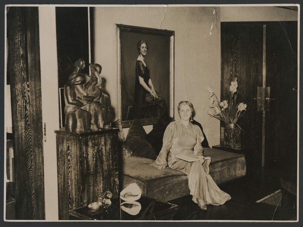 Louise Dyer in a long-sleeved, floor-length gown, seated in her rue Franklin apartment in front of her portrait