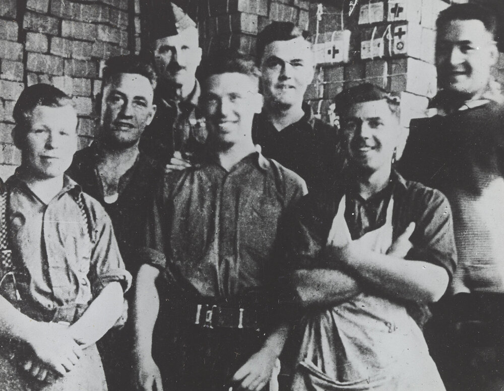 Unidentified prisoners of war camp: Group of men with stacked Red Cross care packages