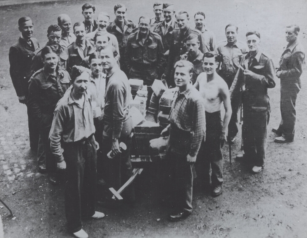 Prisoner of War Camp: British officers at Oflag camp [unidentified] gathererd around a trolley of Red Cross parcels