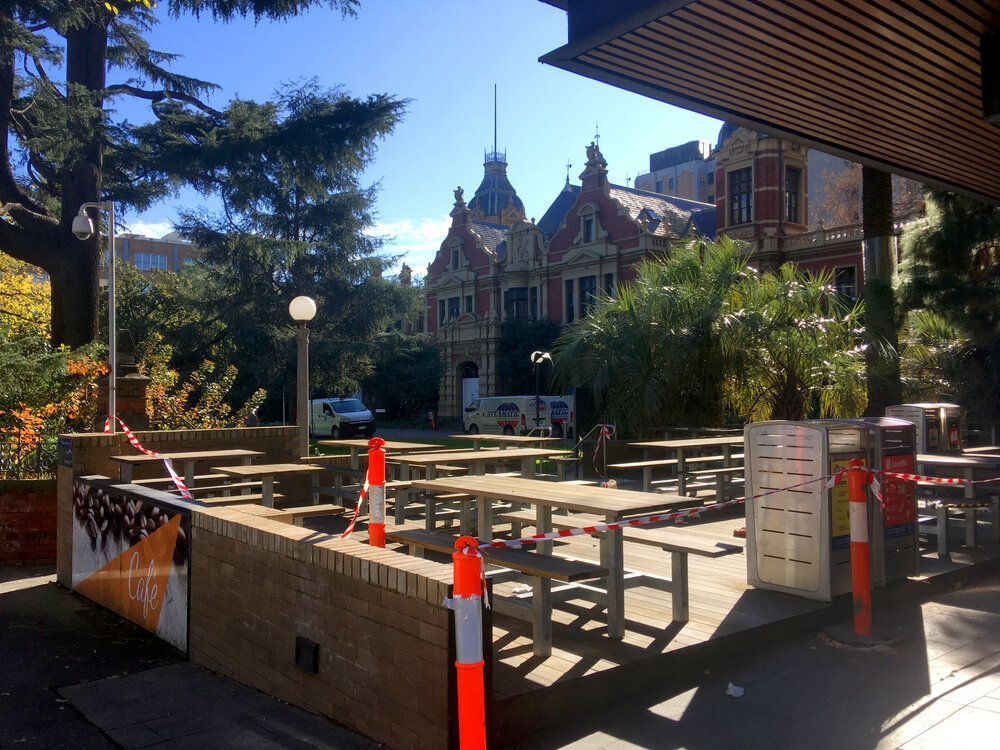 Parkville during COVID lockdown - Brew Sisters CafŽ outdoor seating closed due to level 3 and 4 restrictions with 1888 Building in background