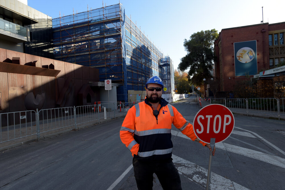 Parkville during COVID lockdown - Construction worker standing on Monash Rd with New Student Precinct construction site in background