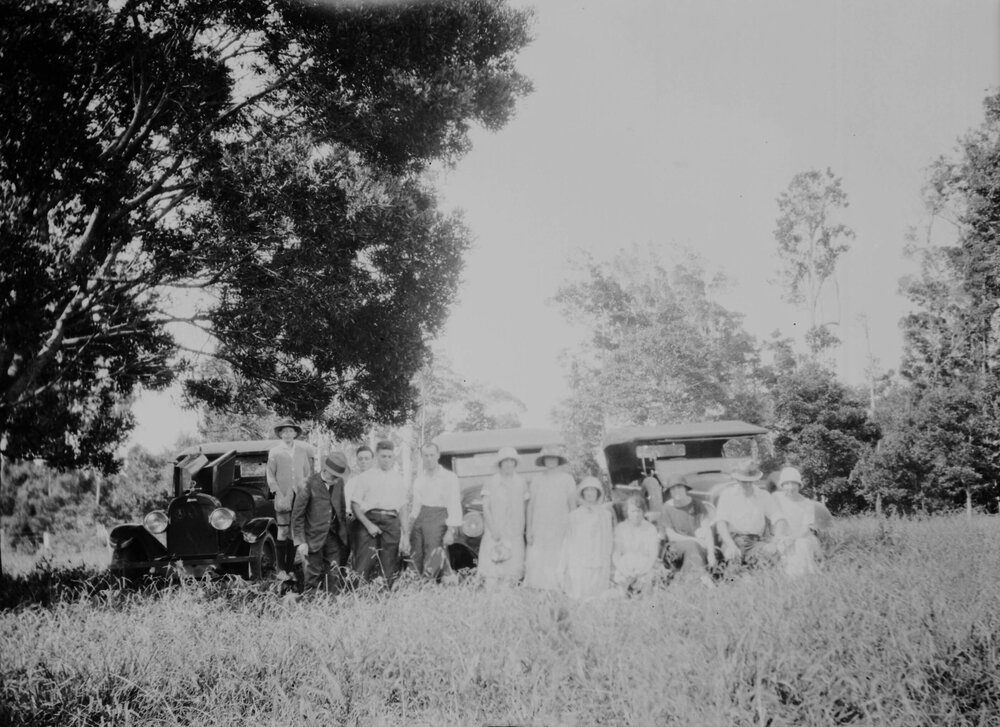 An unidentified group of people in front of cars in a country setting
