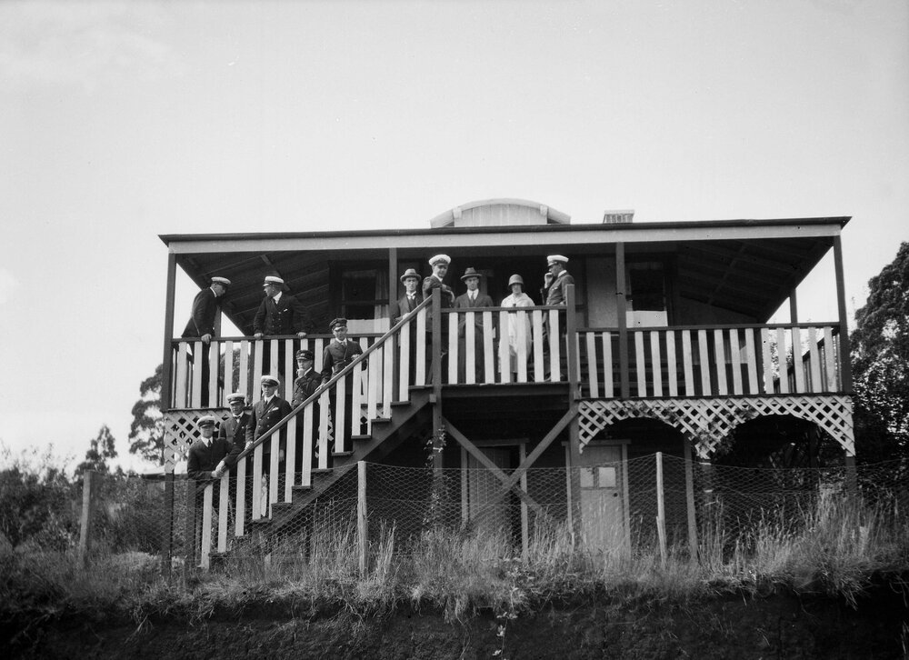 A group of unidentified people - mainly men in naval uniform - on the stairs and verandah of a house in Ferny Creek, Victoria