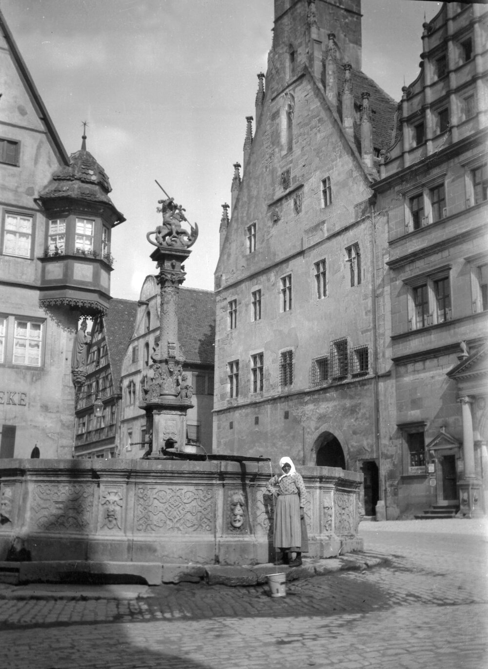 An unidentified woman collecting water from a well in a square in Rothenburg, Dinkelsbuhl or Wurzburg, Bavaria, Germany
