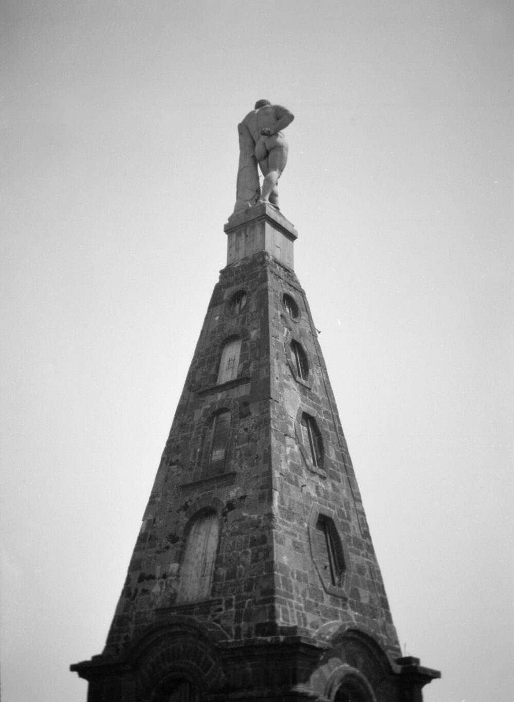 An unidentified statue of a nude man on a spire or pedestal