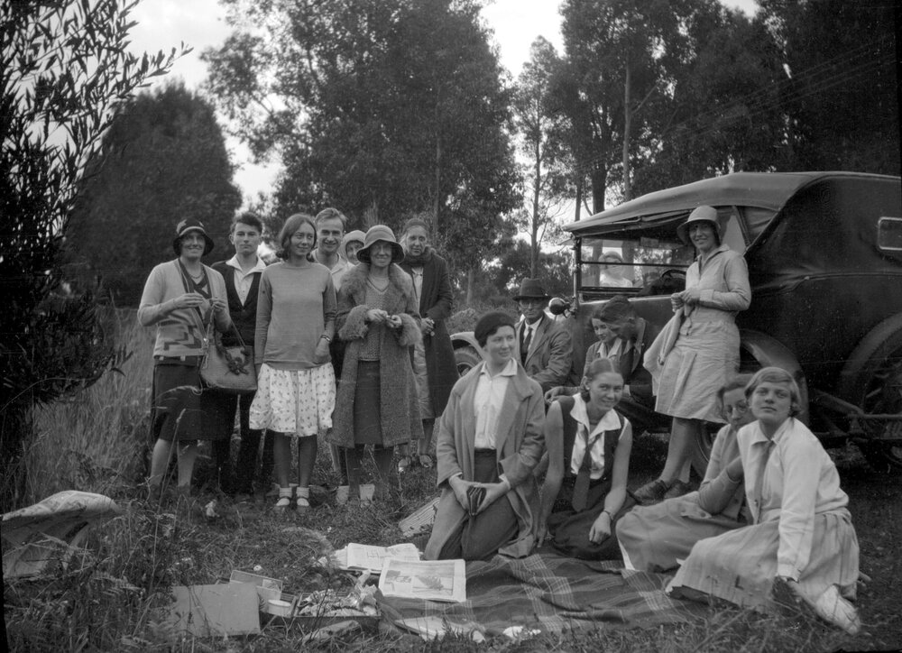 A group of 15 unidentified men and women alongside a car in a bushland setting at Sassafras, Victoria