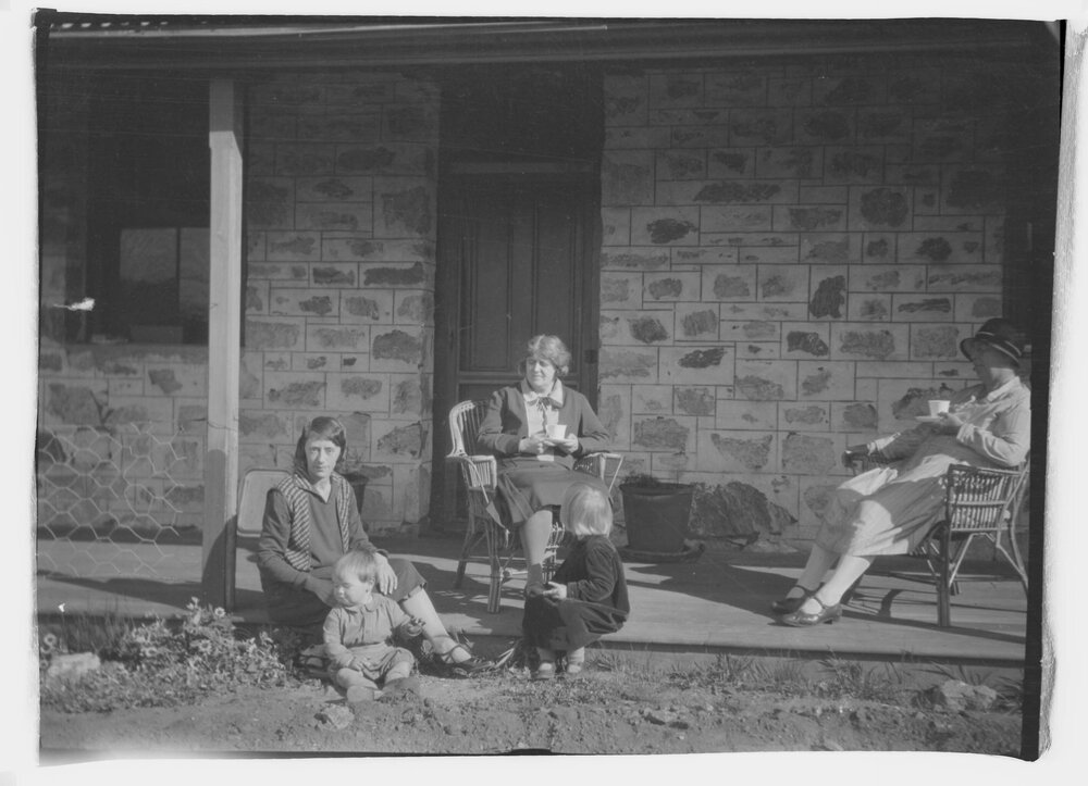 Three women and two young children seated on the verandah of a farmhouse