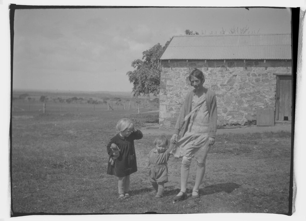A woman and two young children in front of a stone farm building