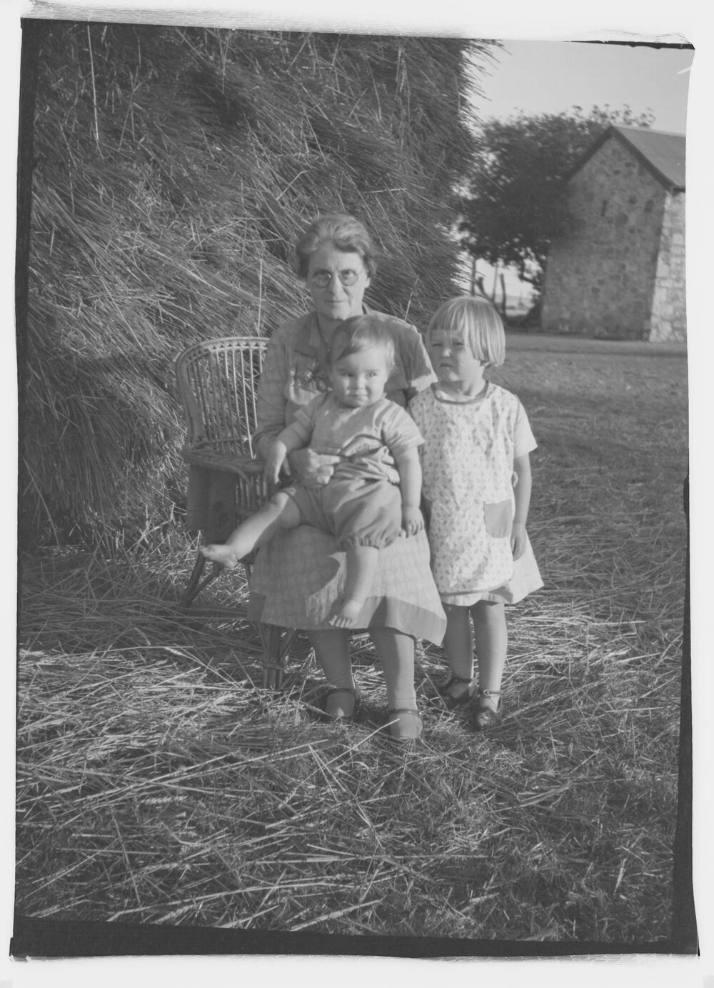 A woman and two young children in front of a hay stack on a farm