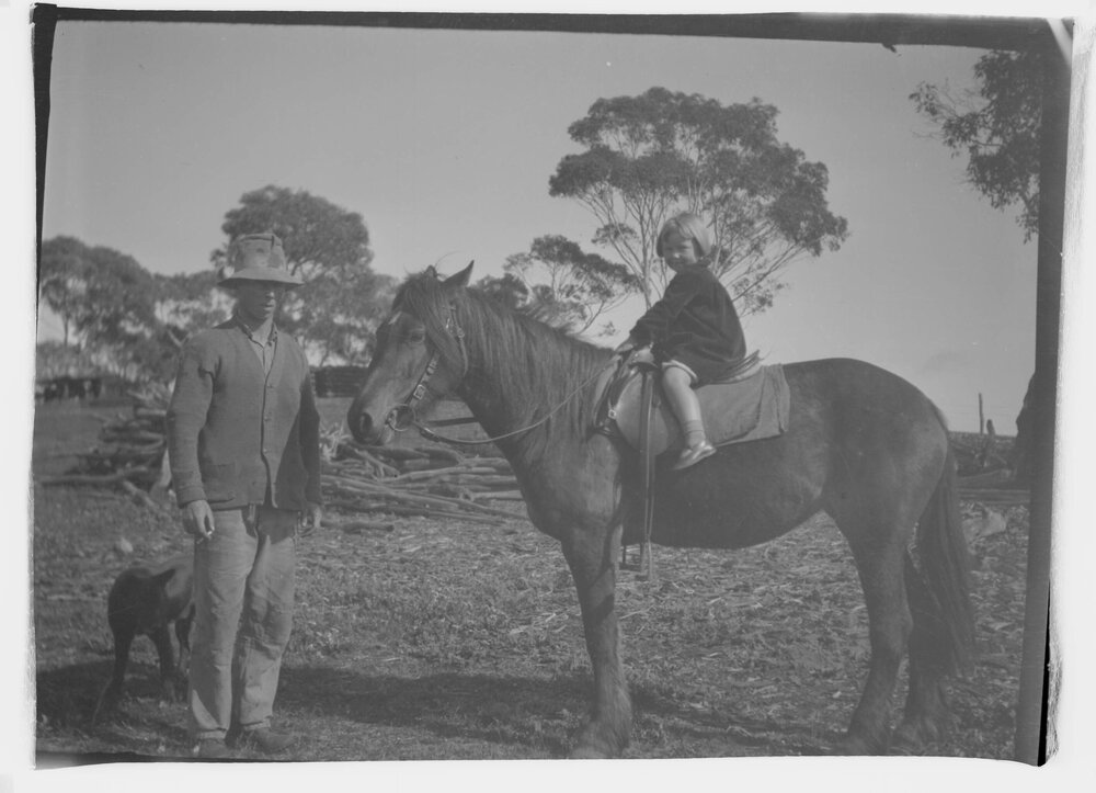 A man standing alongside a young girl mounted on a horse