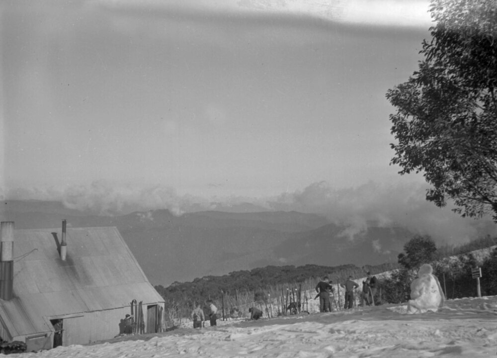 A view of skiers, a ski lodge and mountains, possibly at Mount Feathertop, Victoria