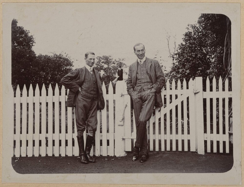 [Two men standing in front of picket fence]