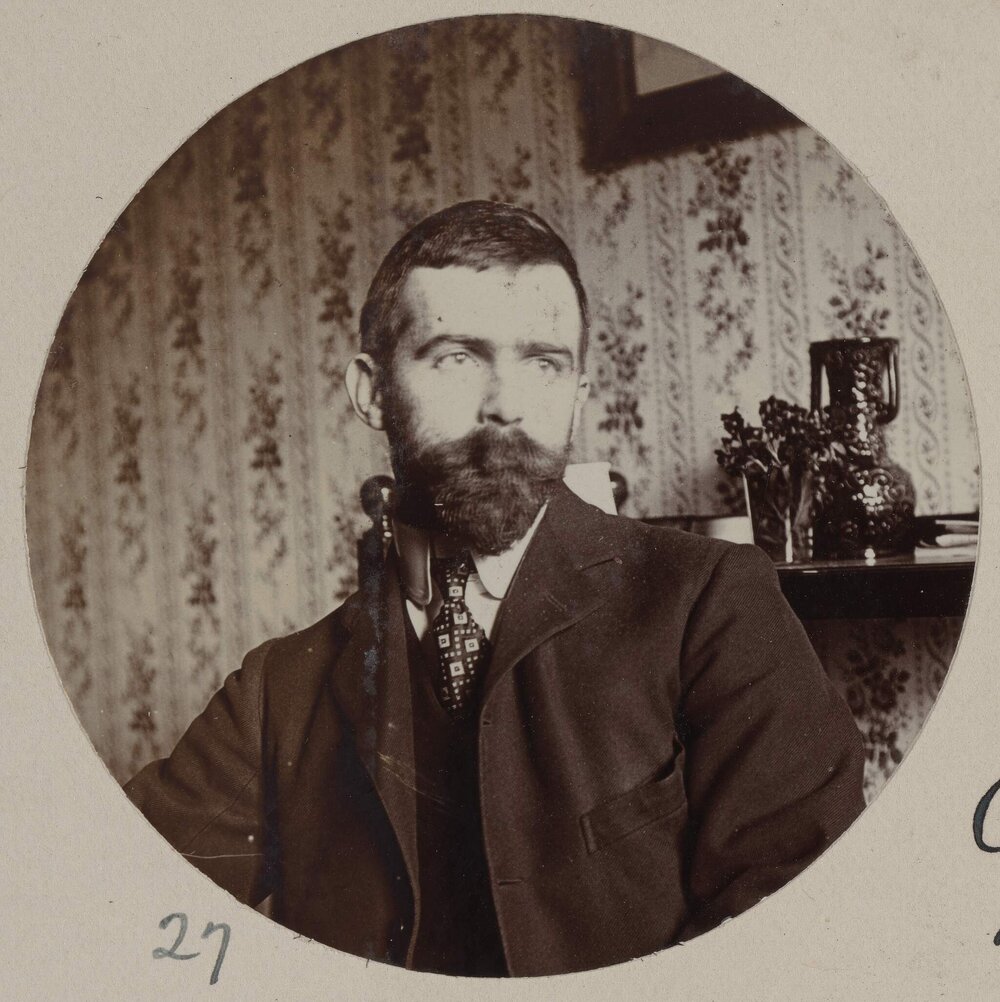 [Seated portrait of man with dark beard]