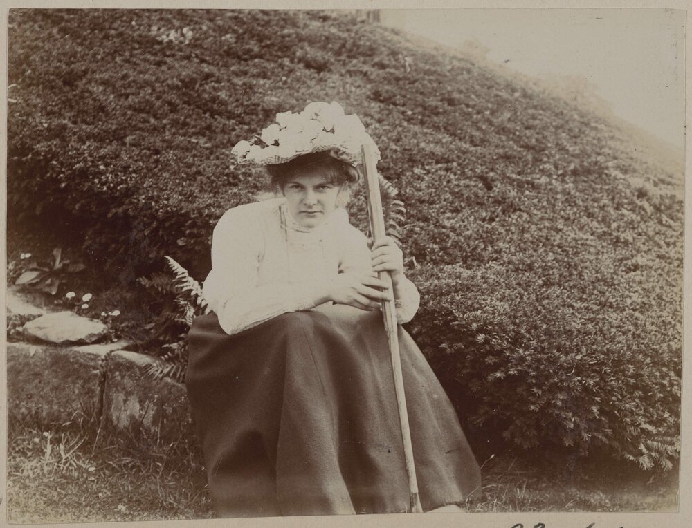 [Woman with flowers on hat seated on rock]