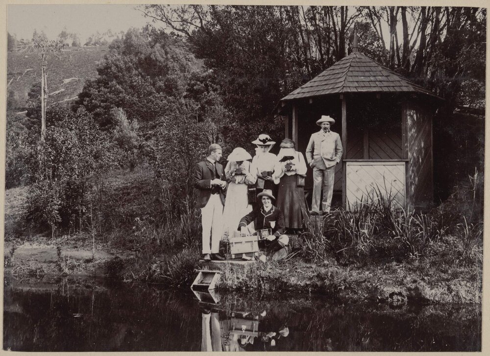 [Group of men and women posing beside lake]