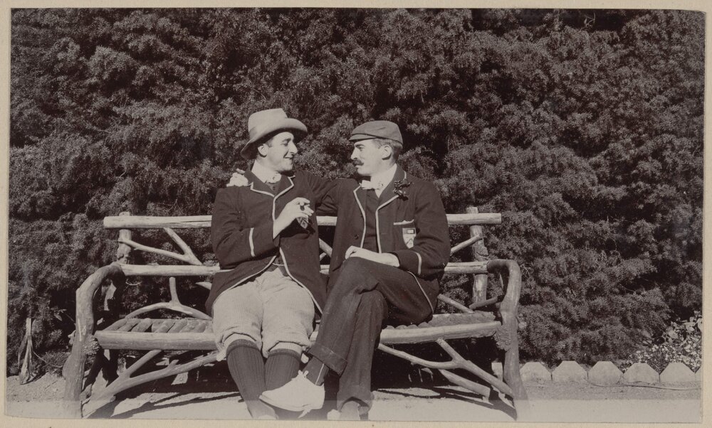 [Two men sitting on bench with log frame]