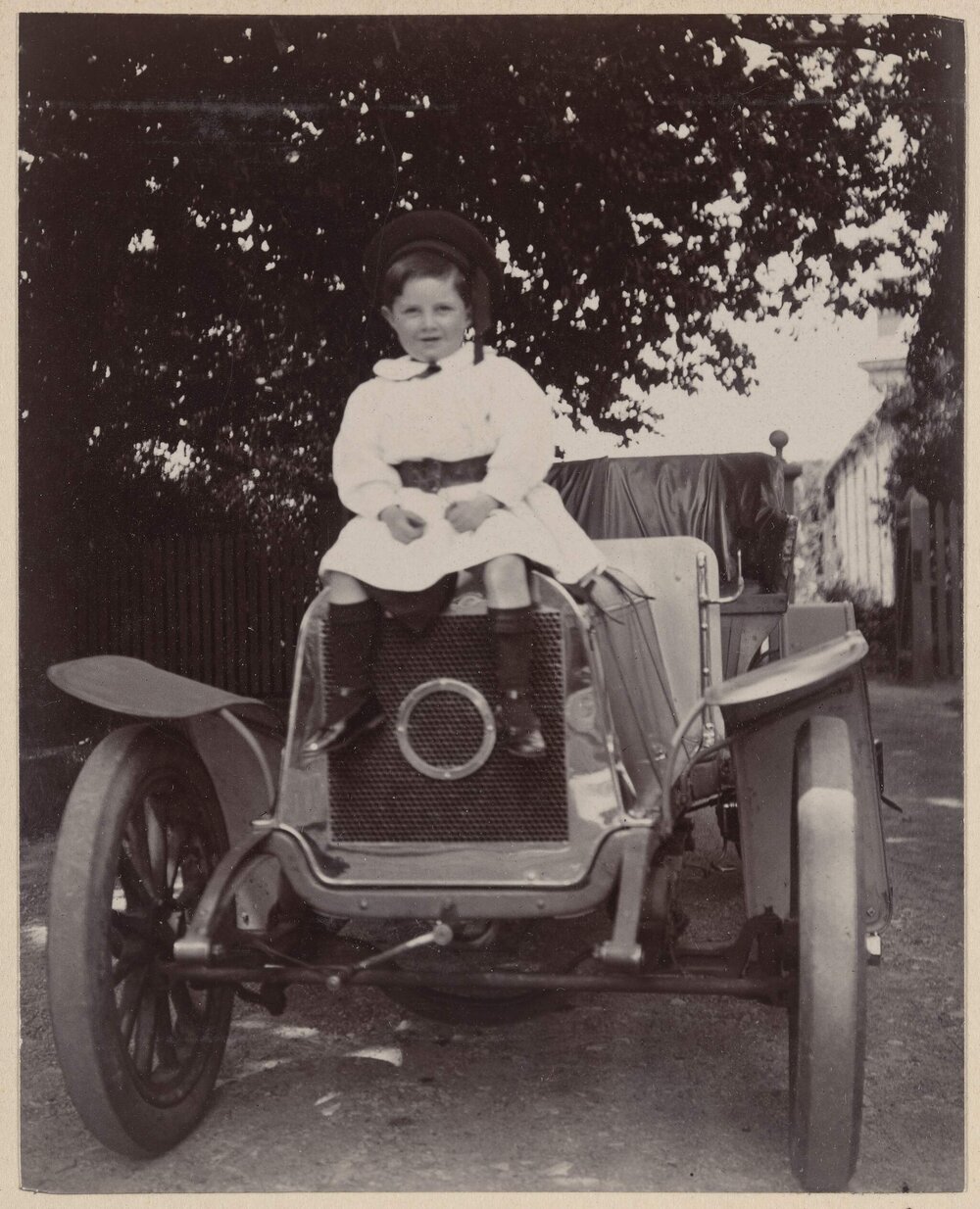 [Young boy sitting of front of motor vehicle]