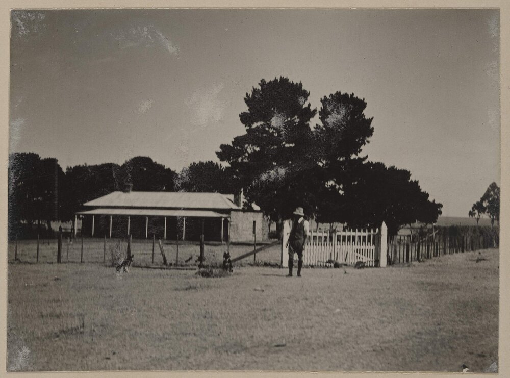 [Man standing at gates to homestead]