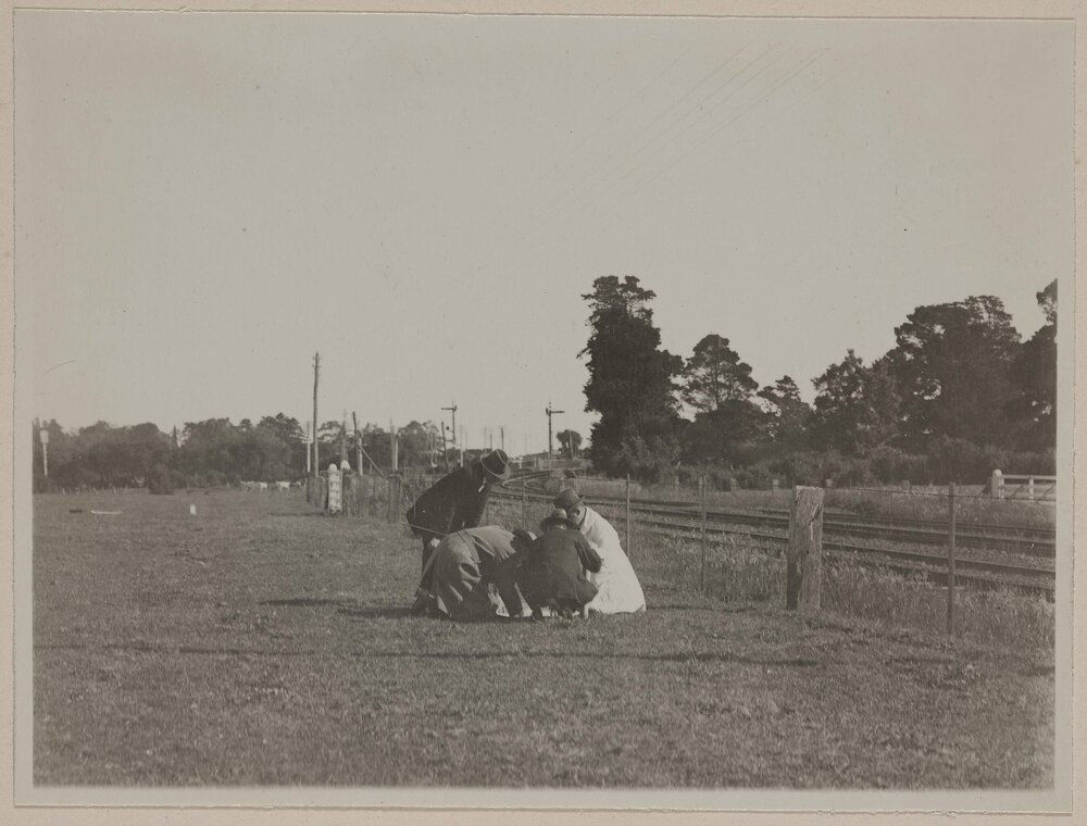 [Four men crouched in paddock near railway line]