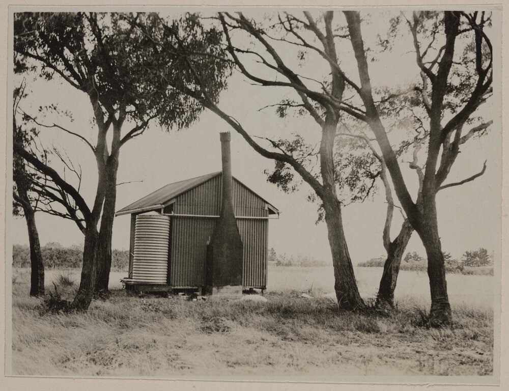 [Exterior of small outbuilding with chimney and water tank]