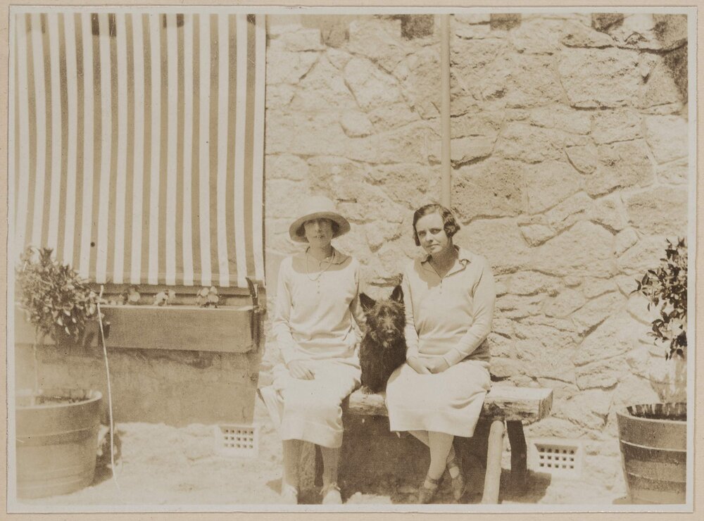 [Two women with dog posed on bench seat]