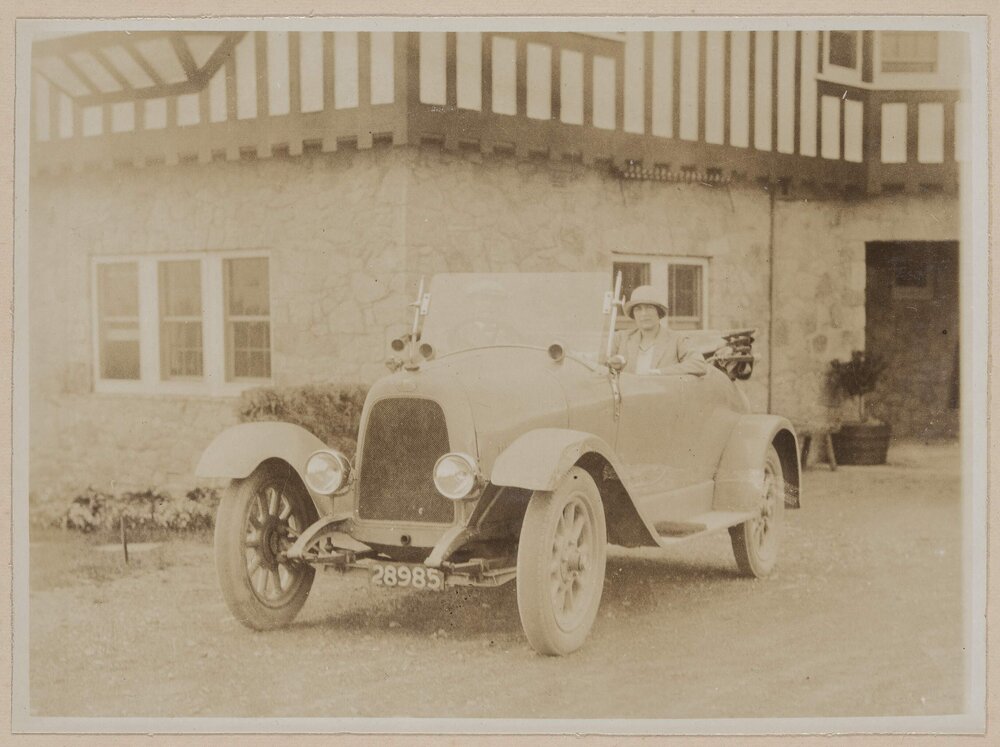 [Woman wearing hat sitting in front seat of motor car]