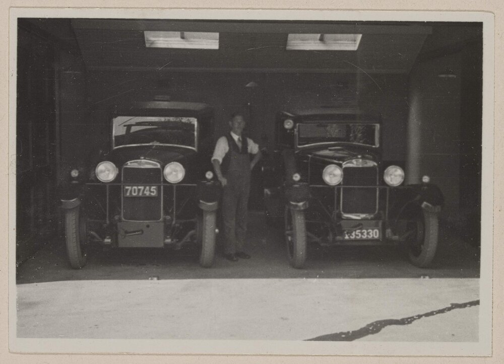 [Man standing between two motor cars]