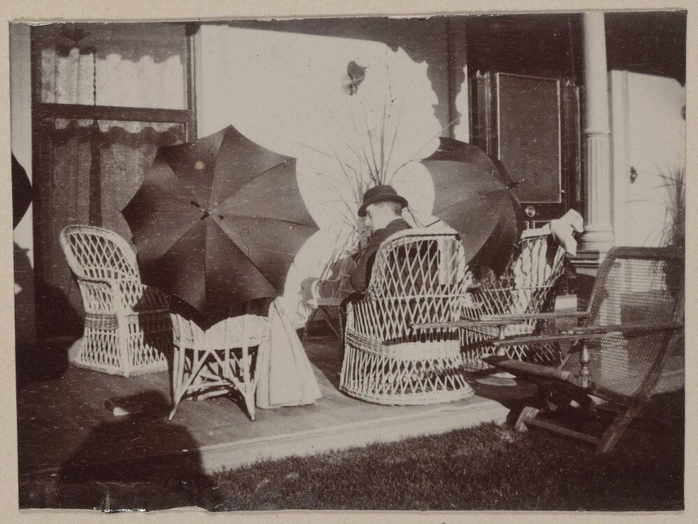 [Seated man and woman holding umbrellas 