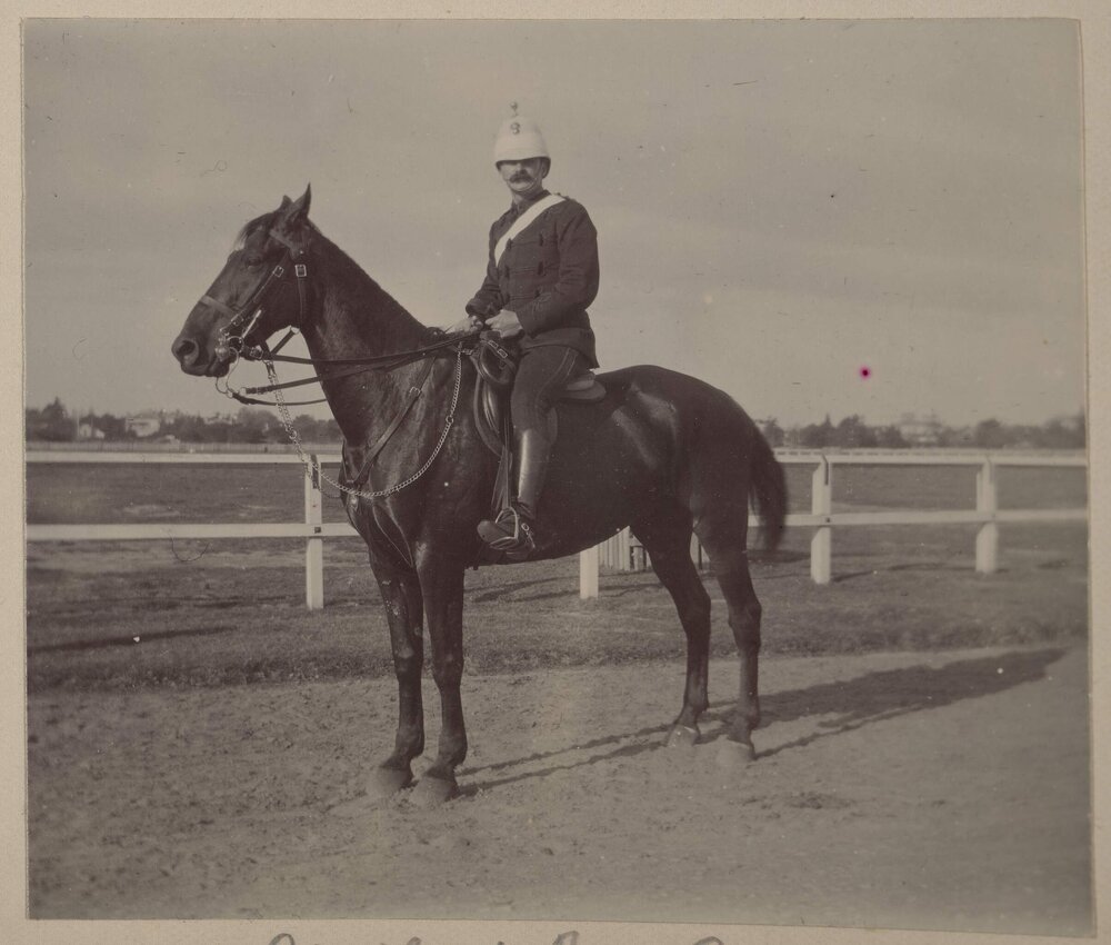 [Man wearing white helmet and tunic seated on horse]