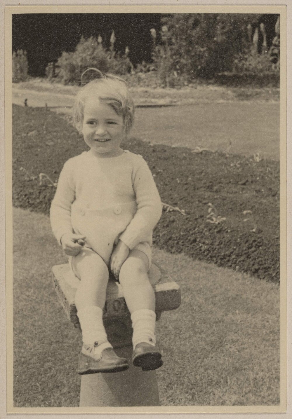 [Toddler seated on garden plinth]