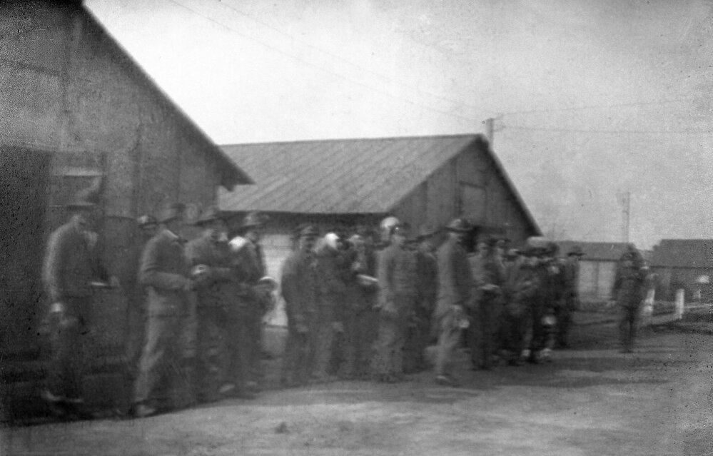 Men gathered in front of timber buildings