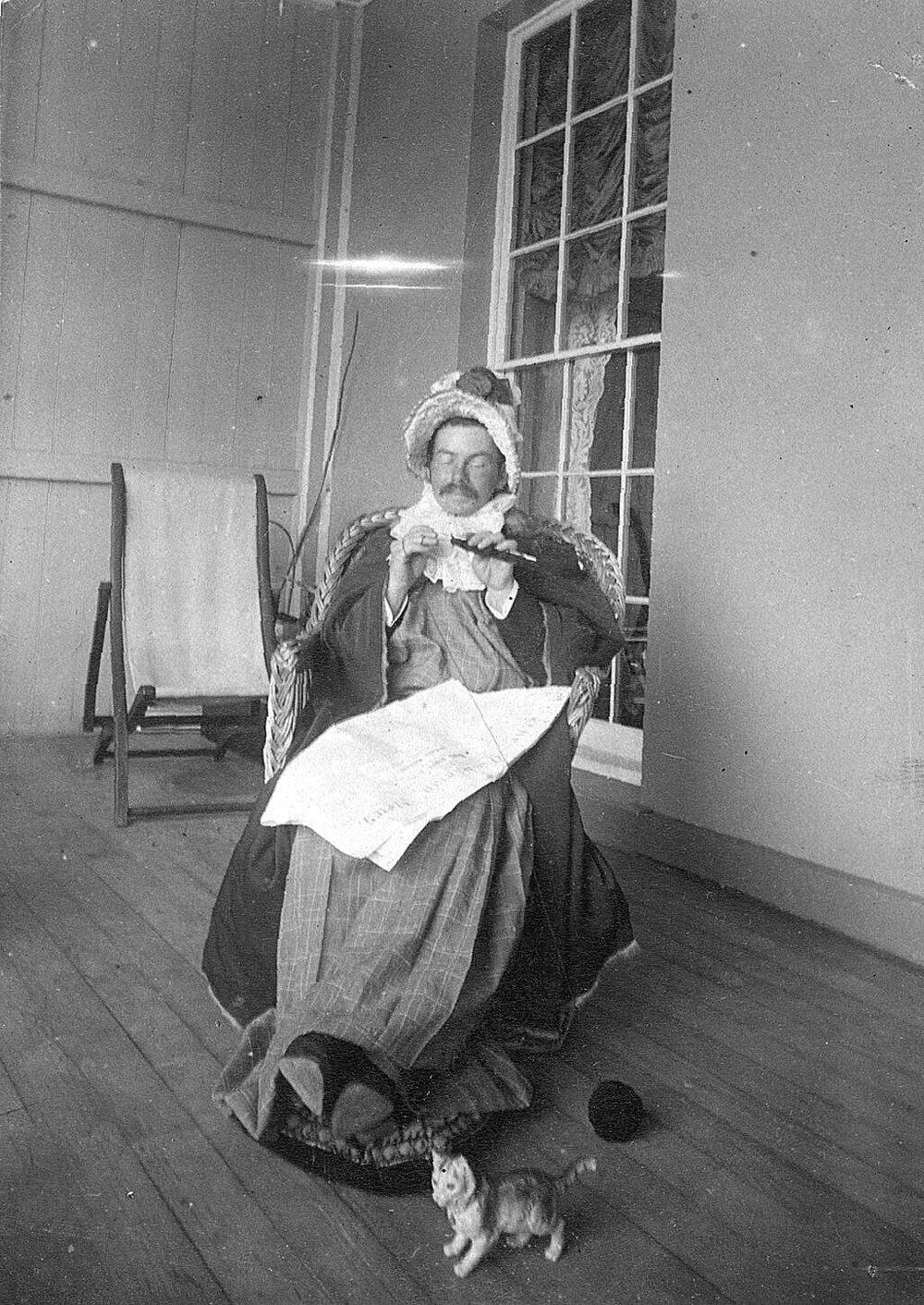 Man dressed in woman's clothing seated on chair