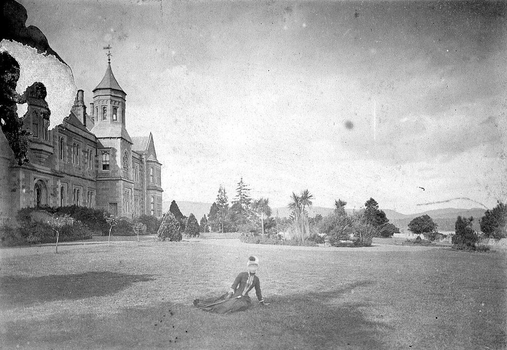 Woman seated on lawn in front of stately home