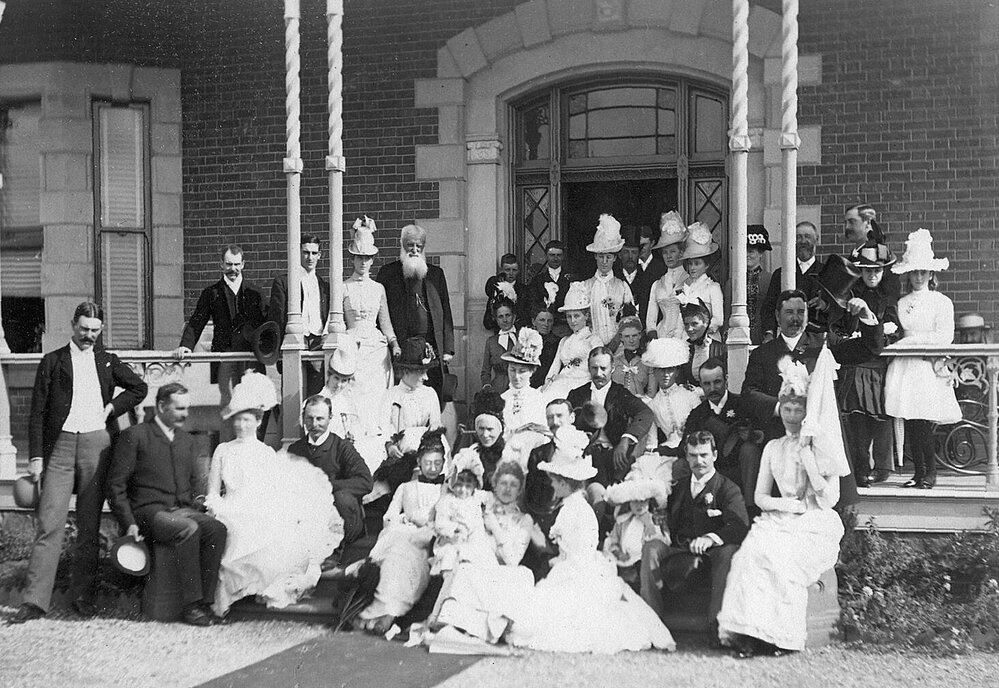Group photo of men and women standing under the verandah of the Purrumbete homestead