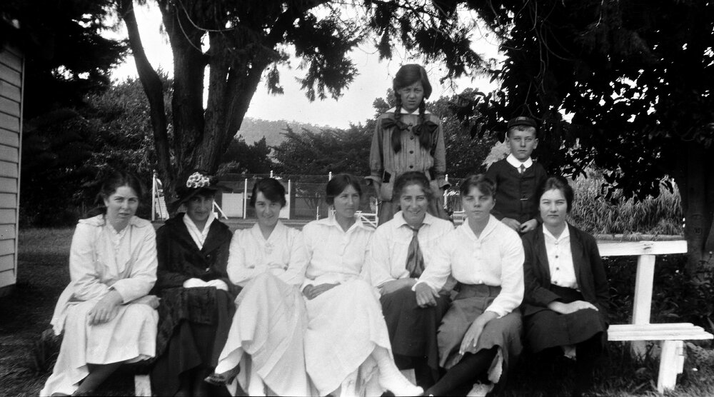 Group of women and a boy sitting under trees