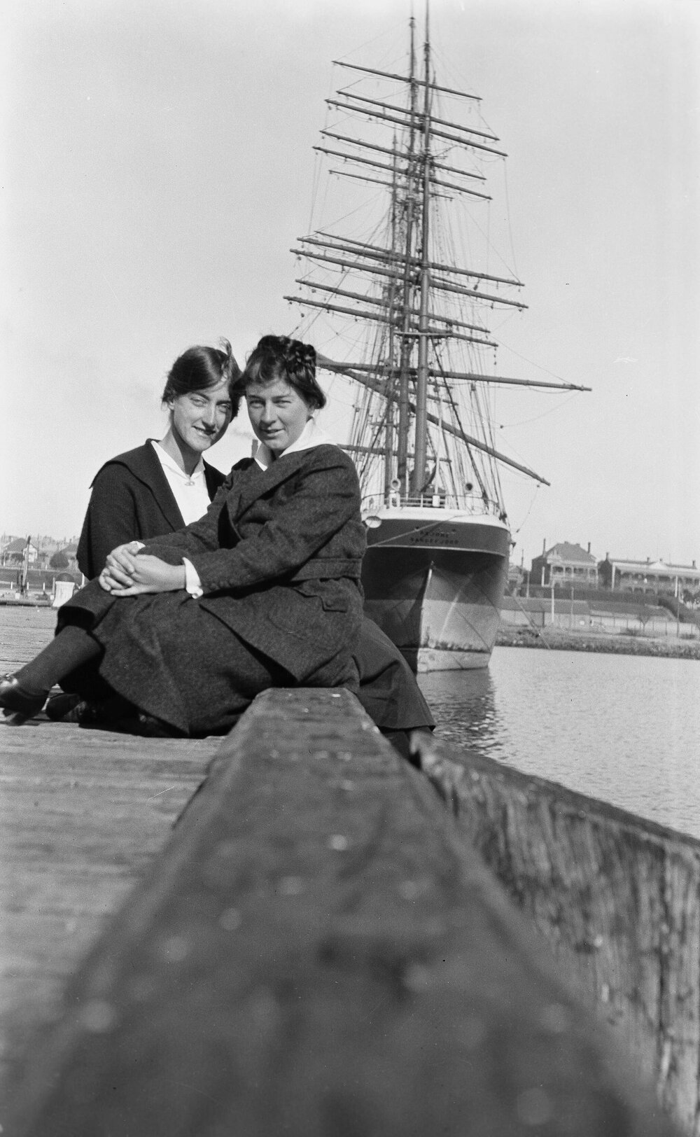 Doris Hall [McKellar] and Pollie Turnbull seated on a quay in front of a ship