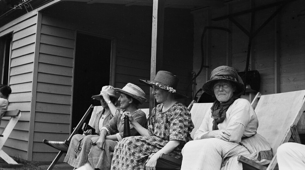Four women wearing hats sitting on deck chairs