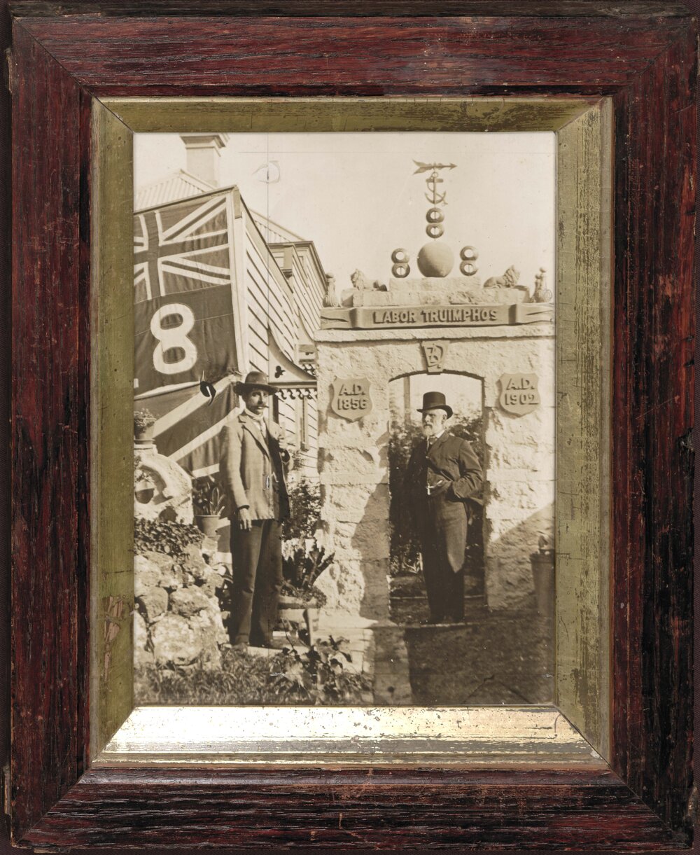 Benjamin Douglass and friend standing under home-built Eight Hours Day monument, inscribed "Labor Triumphos".
