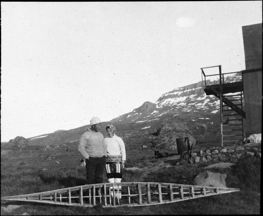 Inuit man and woman stand with a kayak