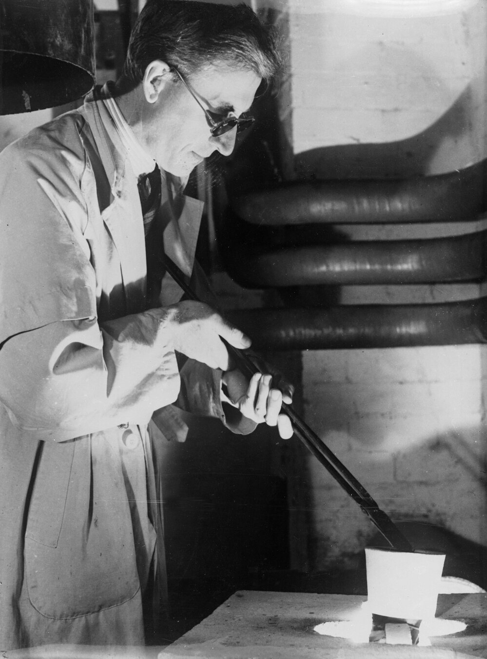 University optical research.  Copy negative of Professor Hartung removing experimental pot of glass.