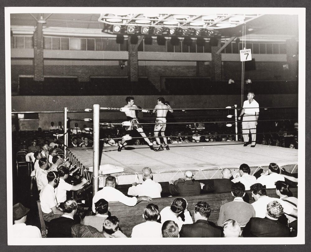 [Photograph of a boxing match taking place inside a ring]
