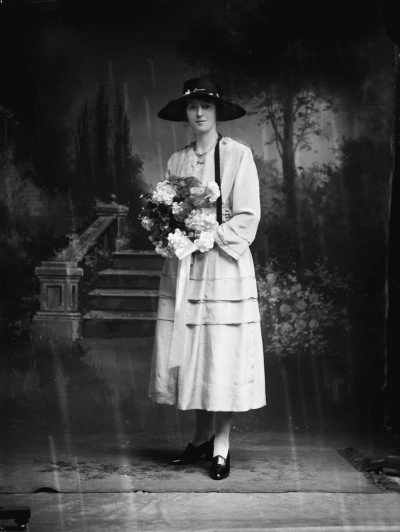 Studio portrait of Miss Scott wearing a black hat and holding flowers.