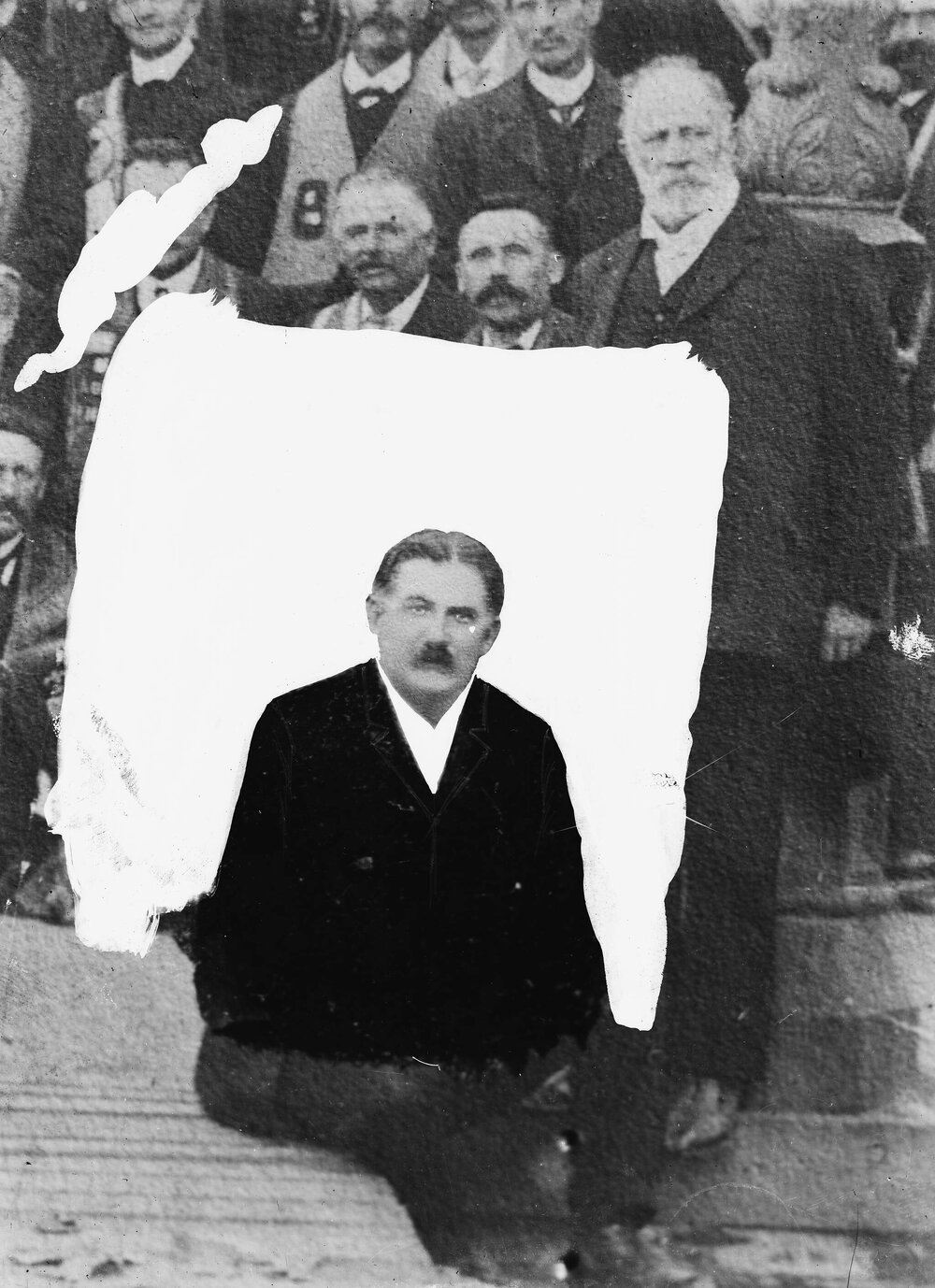 A group of men.  One unidentified man has been masked out from the rest.