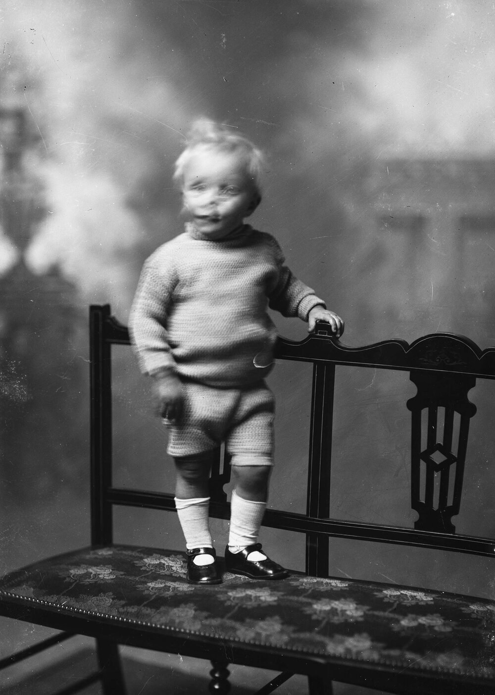 Studio portrait of an unidentified boy standing on a bench.