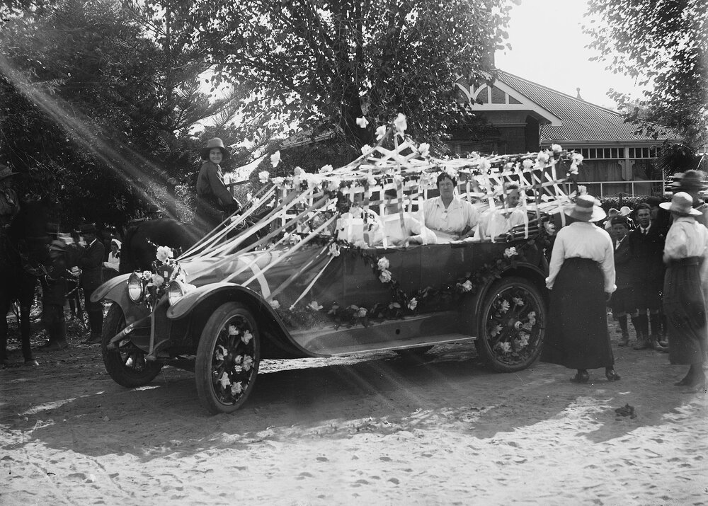 An open car, heavily decorated with flowers and streamers, and carrying several women.
