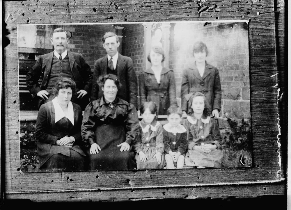 An unidentified group of nine people in front of a brick building.