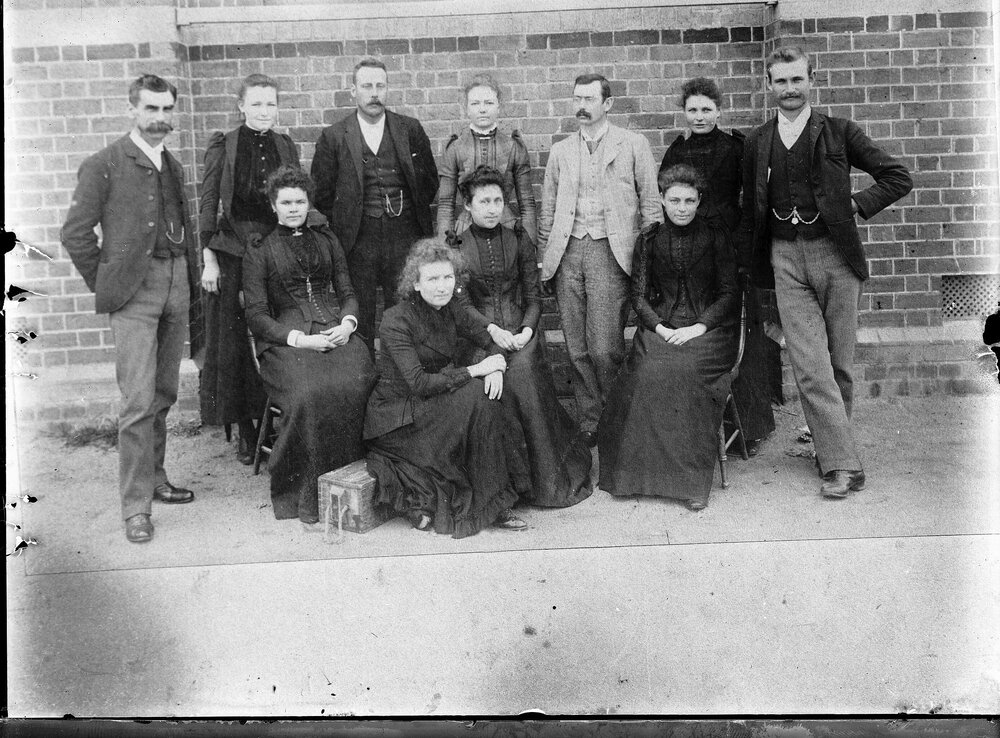 A posed group of unidentified people in front of a brick building.