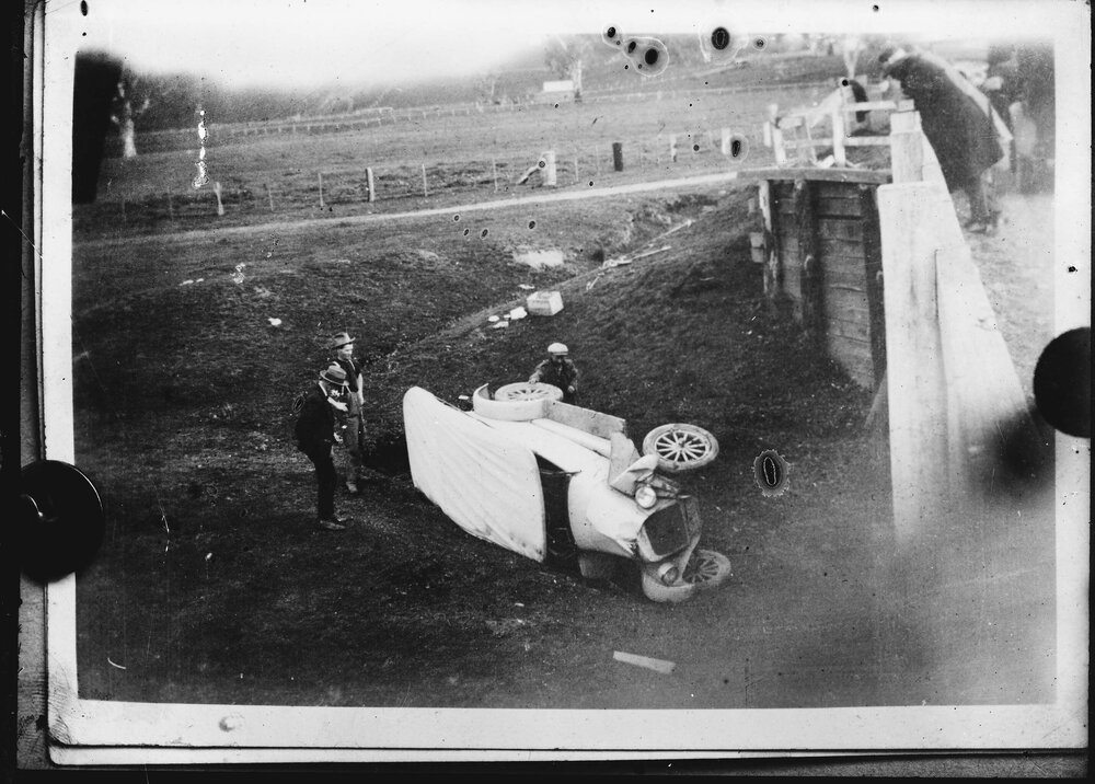 A damaged car beneath a bridge.