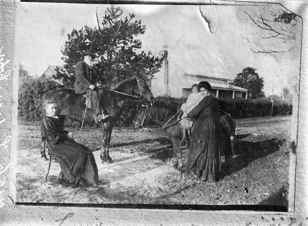 People and horses outside a timber cottage.