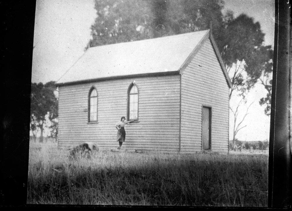 An unidentified woman standing outside a small public building.